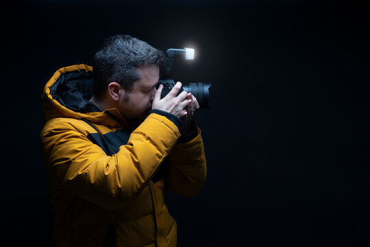 Photographer in a yellow coat taking a photo with flash with a black background