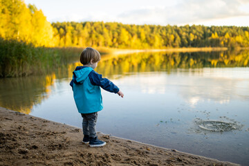 Adorable toddler boy having fun by the Gela lake on sunny fall day. Child exploring nature on autumn day in Vilnius, Lithuania.