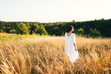 Brunette young woman in wild field. Natural beauty and romance concept. Sunset light. View from the back.