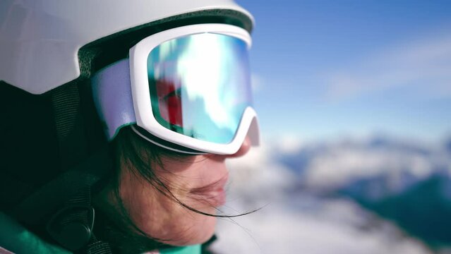 Close-up portrait of woman snowboarder skyer in ski helmet and glasses in mountains, side view. Girl wearing in ski clothes in winter resort. Enjoy healthy sport active rest, snowboarding lifestyle. 