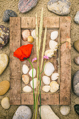 Bilderrahmen aus Treibgut im Sand mit Muscheln, Steinen und Blumen dekoriert liegt am Strand im Urlaub