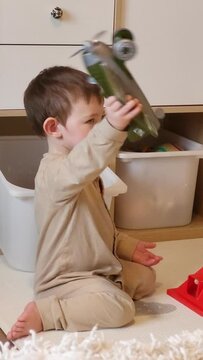A happy child is playing with toys sitting on the floor in the nursery. Baby smiles while playing games at home. Kid aged one year eight months (20 months)