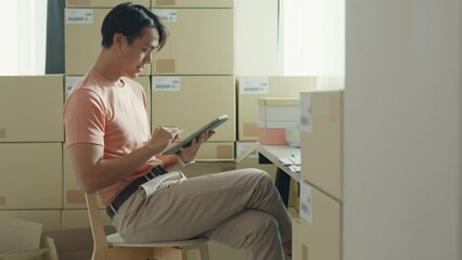Young Asia male entrepreneur small business confirm purchase order from customer parcel barcode tracking number on digital tablet check inventory product ready shipping at small online retail shop.