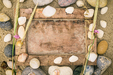 Bilderrahmen aus Treibgut im Sand mit Muscheln und Steinen dekoriert liegt am Strand im Urlaub
