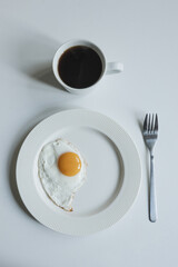 A light breakfast on a white table, a fried egg, and black coffee.