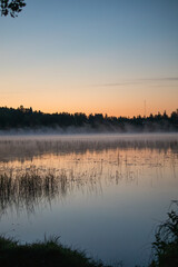 Sunrise on a misty still lake in summer countryside.
