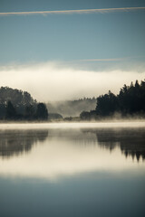 Lake scenery with a misty clouds reflecting over a forest horizon.
