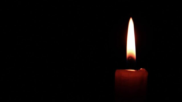This stock video shows a burning candle against a black background