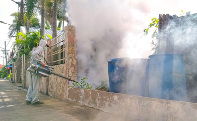 Healthcare worker using fogging machine spraying chemical to eliminate mosquitoes and prevent dengue fever on overgrown in public area