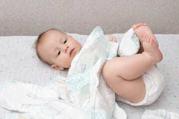 A baby in a diaper lies on a white background plays with a stack of diapers. Copy space for text