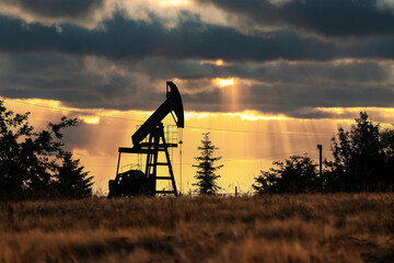 Oil pump against incredible orange sunset sky. Industrial concept. Pump jack silhouette on evening...