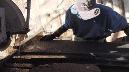 Latino person cutting a plate of natural volcanic stone on a work table inside the workshop, with water to facilitate cutting, protection to avoid damage