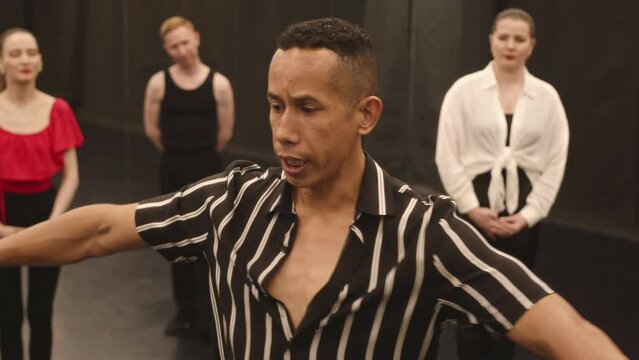 Medium slowmo of Hispanic male dance teacher showing Latin dance movements to group of people attending his master class in studio
