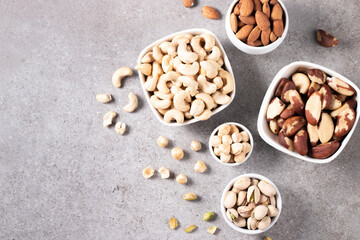Large assortment of nuts in different bowls on stone table.