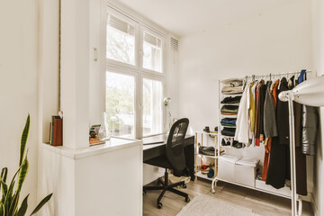 a room with a desk, chair and clothes hanging on the wall behind it is a large window that looks out onto the street