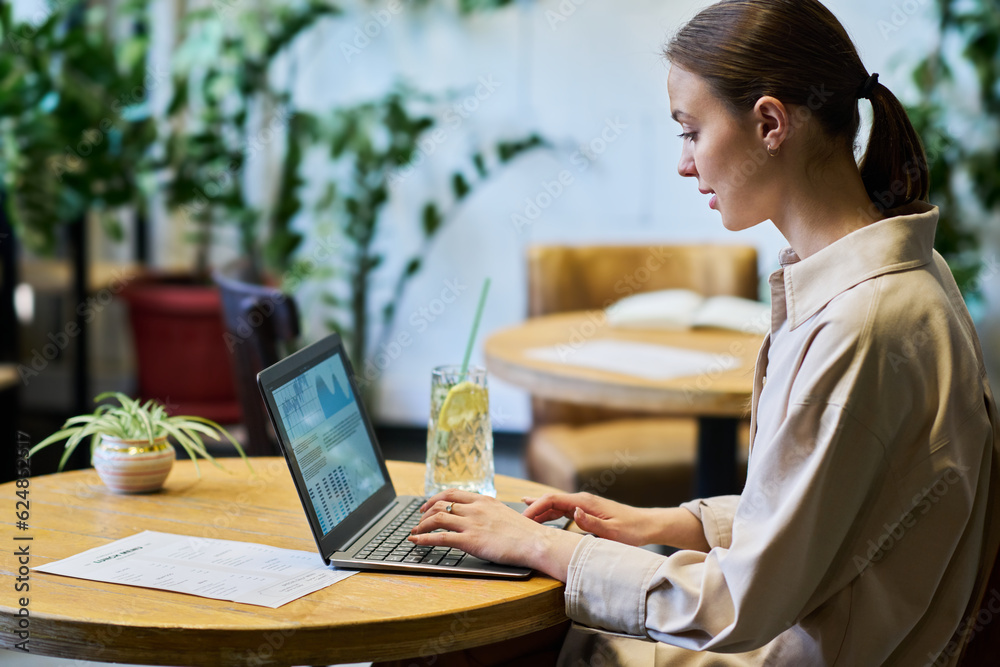 Poster side view of young female economist or broker analyzing online financial data on laptop screen while