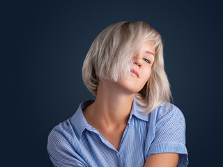 Portrait of a young female model with blonde hair. A girl with big blue eyes, plump lips. Looking into the camera, posing against the black background of the studio.