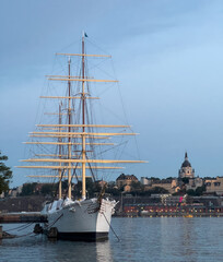 Stately tall ship sits at dock with Stockholm skyline in the background.