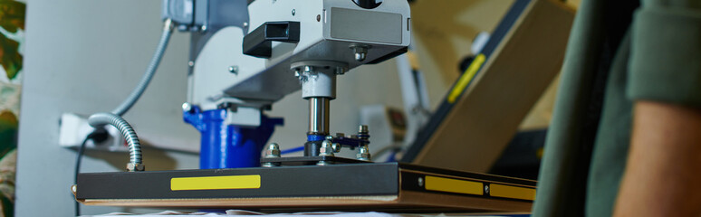 Cropped view of blurred young craftsman standing near screen printing machine in print studio, customer-focused small business concept, owner-operated, print studio, banner