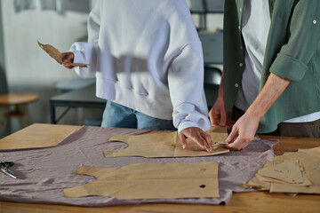Cropped view of young african american craftswoman holding sewing pattern near colleague and fabric on table in print studio, collaborative business owners working together