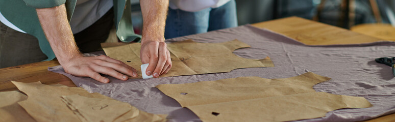 Cropped view of craftsman marking cloth near sewing patterns and blurred colleague while working in print studio, collaborative business owners working together, banner