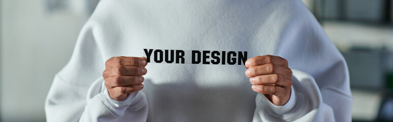 Cropped view of young african american designer in sweatshirt holding printing layer with your design lettering in print studio, focused business owner managing workshop, banner