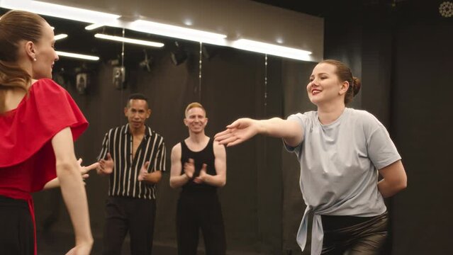 Medium slowmo of expressive young beautiful women dancing Latina and men watching and clapping while having group dance class in studio