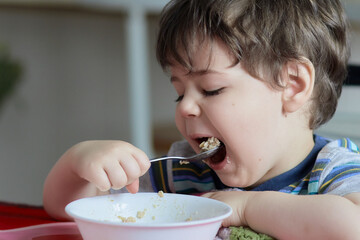 cute young boy eating healthy oatmeal for breakfast - obrazy, fototapety, plakaty