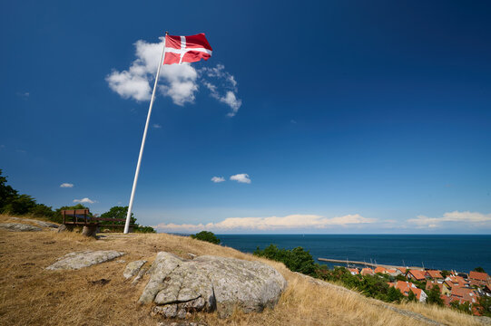 D&auml;nische Nationalflagge Danebrog weht im Sommerwind &uuml;ber der d&auml;nischen Stadt Gudhjem auf der Ostseeinsel Bornholm vor blauem Himmel