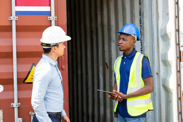 Logistic foreman discussing business work with African contractor worker at container warehouse or construction site.