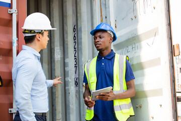 Logistic foreman discussing business work with African contractor worker at container warehouse or construction site.