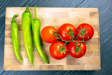 red tomatoes and green hot peppers on a kitchen board