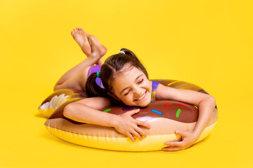 Cute little girl in swimsuit with inflatable ring on yellow background. Summertime kids activity...