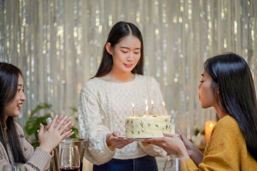 Cheerful friends enjoying home Birthday holiday party. Asian sister cheering drinking red wine celebrating with Birthday cake.