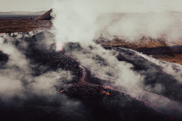 Aerial shot of a lava field of an active volcano and burned moss with a lot of smoke.