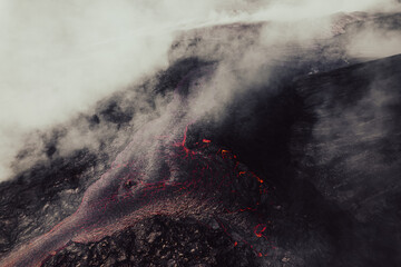 Aerial shot of flowing lava with a lot of smoke of the active volcano.