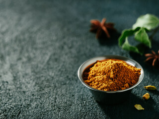 Indian or pakistani masala powder and spices on dark textured background. Small metall bowl with...