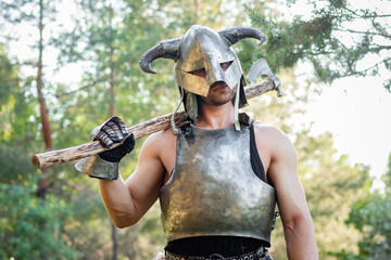 Portrait of a warrior in a horned helmet, a steel breastplate with a two-handed ax in his hands,...