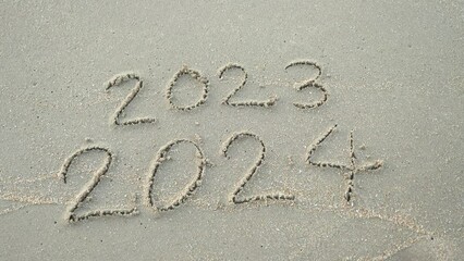 Message Year 2023 replaced by 2024 written on beach sand background. 
Goodbye 2023 hello to 2024 Lapping waves happy New Year coming concept.