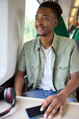Young Man Commuting To Work Sitting  On Train With Wireless Headphones And Mobile Phone