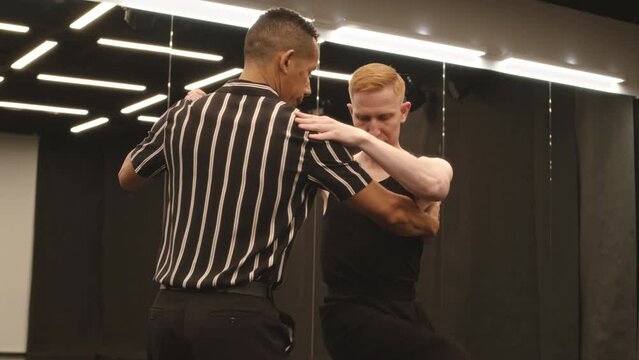 Medium slowmo of two young handsome multiracial male ballroom dancers dancing in pair in spacious mirrored studio