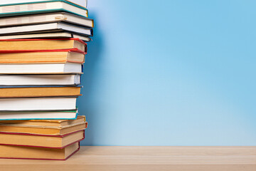 Stack of books in the colored cover lay on the wooden  table and blue backround. Education learning concept