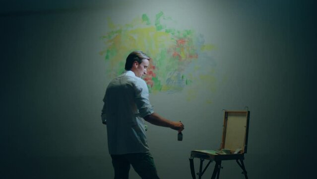 Good looking artist man painting a modern painting on the wall on his art studio he using oil colour and paint brush