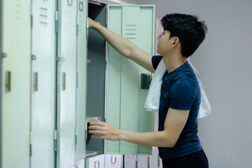 Fototapeta na wymiar An asian young man in blue t shirt and black short retrieves item from his locker. He pick somthing from locker gym.
