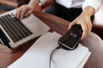 Woman charging mobile phone with wireless fast charger pad on desktop.