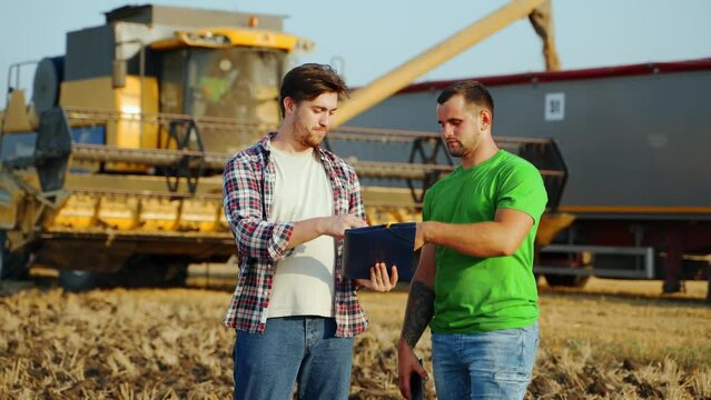 Farmer, logistics agent talk on grain supply agreement in wheat field. Agronomist discuss agriculture business contract. Rancher, landlord negotiate. Harvester loads truck. Global food hunger crisis.