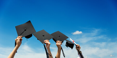 Many hands holding graduation hats against blue sky