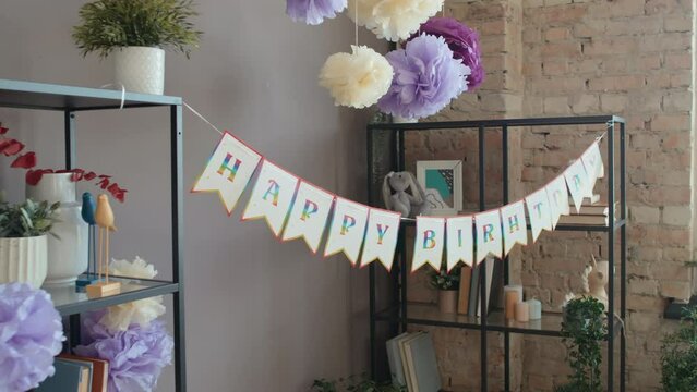 Close-up shot of happy birthday bunting and paper pompoms in loft-style minimalist living room of family home before arrival of guests for party