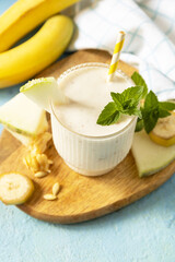 Banana smoothie with melon in drinking glass on wooden board on a stone background. Detox menu. Fresh seasonal smoothies. Copy space.