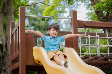 Obraz premium Asian young kid playing on yellow slider at playground with smile of happiness and open his arm like a wing of plane.
